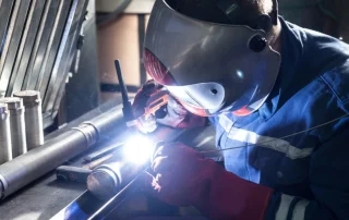 Soldador con careta y guantes realizando soldadura TIG sobre una pieza tubular